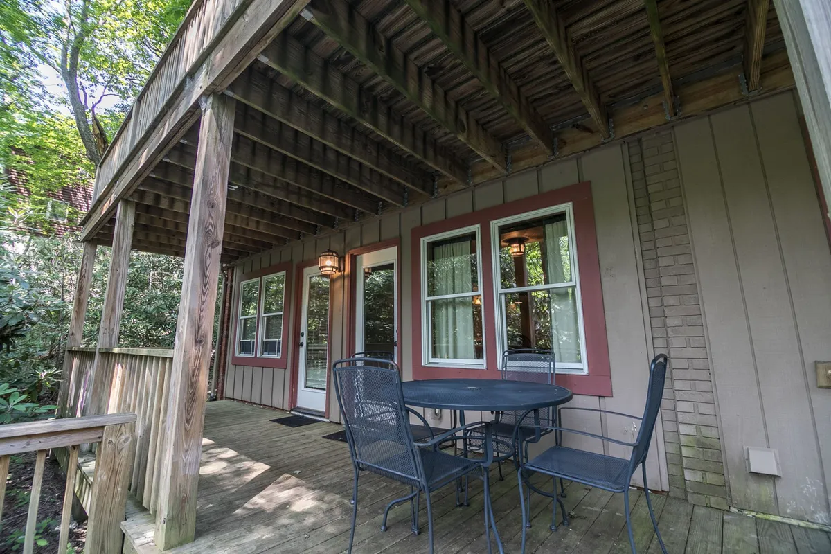 An inviting outdoor deck with wooden beams offers a cozy space for morning coffee or evening gatherings. The scene includes a table and chairs, with tree-filled views enhancing the sense of immersion in nature.