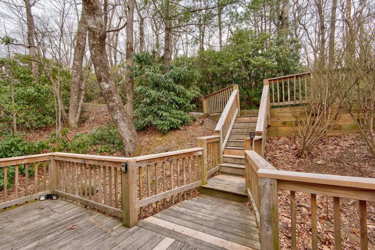 Wooden stairs lead through lush natural greenery, bordered by a sturdy wooden railing. The angle suggests movement from the house to the surrounding forest, inviting outdoor exploration and easy access to nature trails—ideal for daily walks with pets.