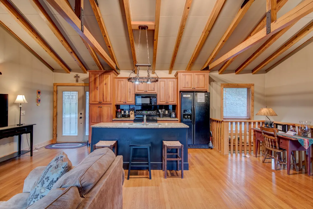 Open-plan interior featuring a kitchen island, wooden beams, stools, a dining area, and a comfortable sofa. The space feels bright, communal, and adaptable, making it welcoming for whole families—including pets—to eat, play, and relax together.