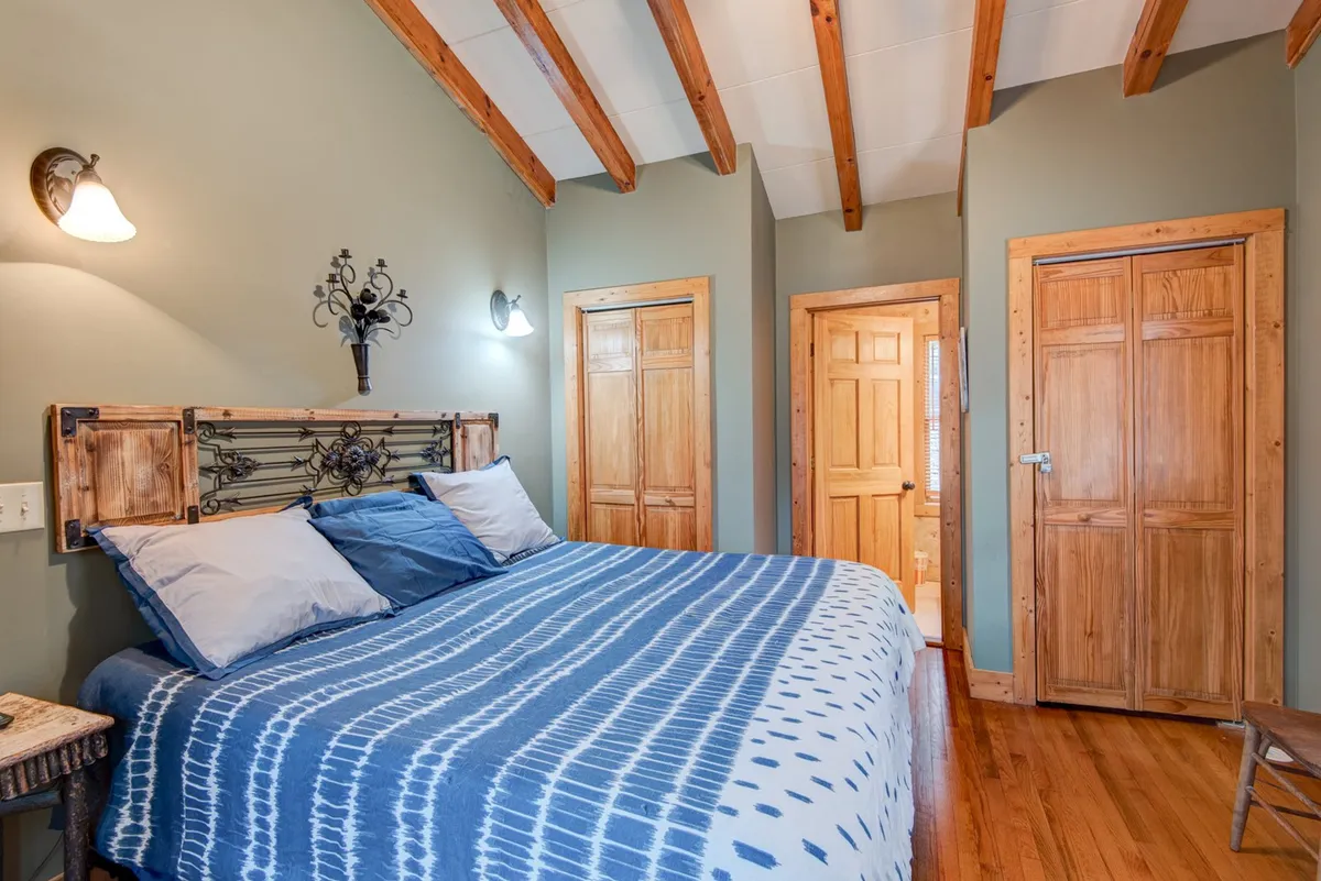 A tranquil bedroom featuring a bed with blue and white linens, a sturdy wooden headboard, and wooden doors in the background. The room is bathed in natural light, suggesting a peaceful retreat ideal for rest and relaxation.