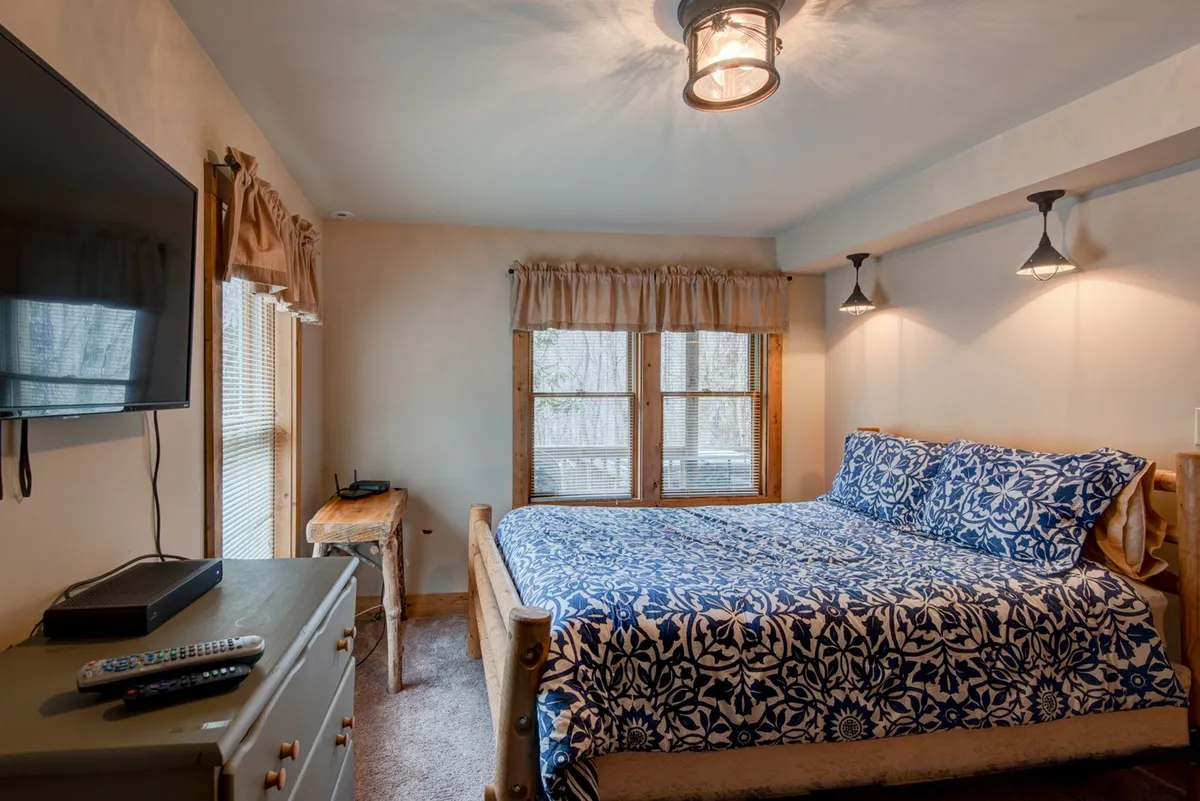 A comfortable bedroom with a blue floral bedspread, wooden furniture, and a TV mounted on the wall. The room feels inviting and bright, suggesting a cozy space for guests to unwind and enjoy entertainment.