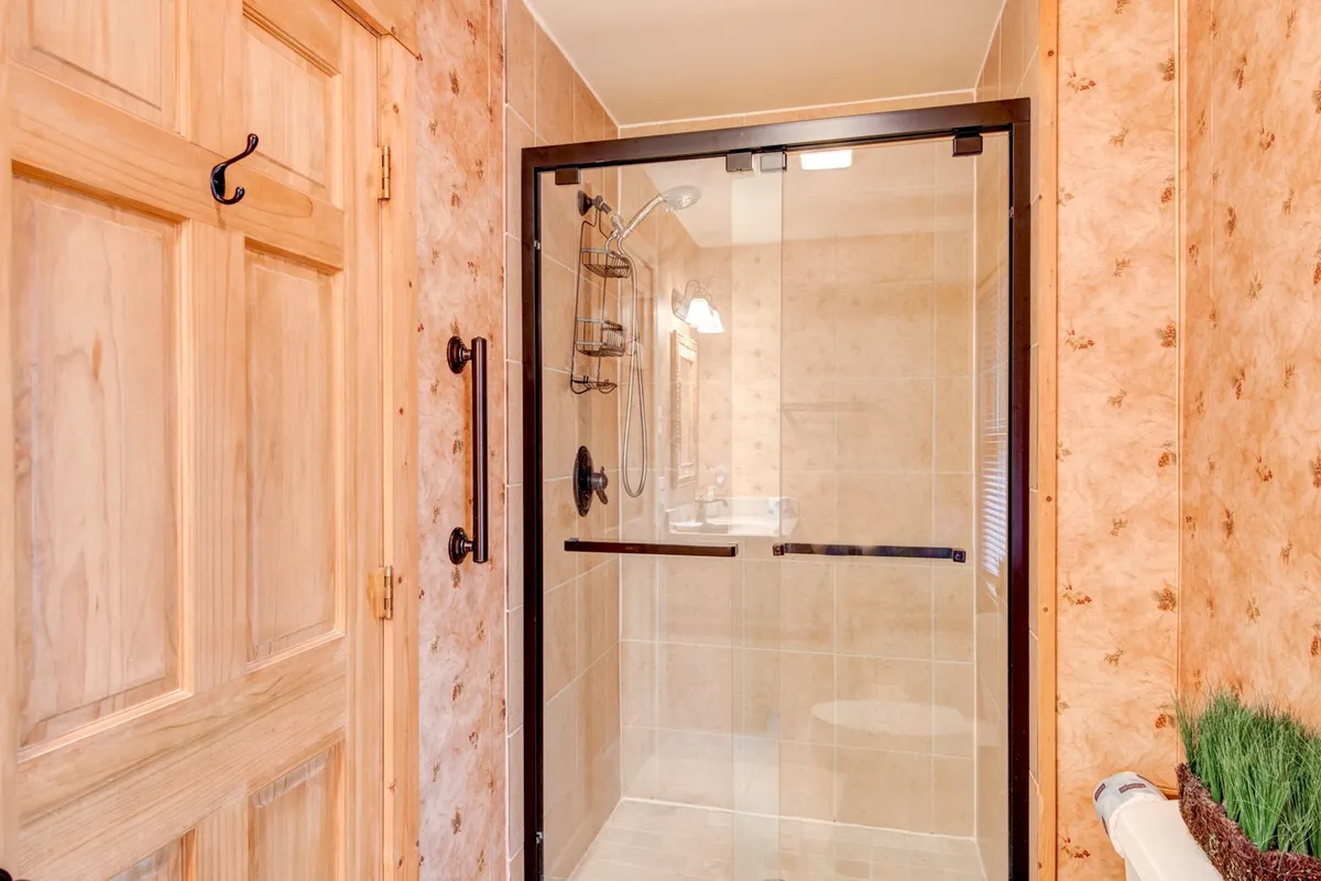 A well-appointed bathroom featuring a glass shower enclosure, a wooden door, and decorative wall texture. The space exudes spa-like serenity, perfect for unwinding after a busy day outdoors.