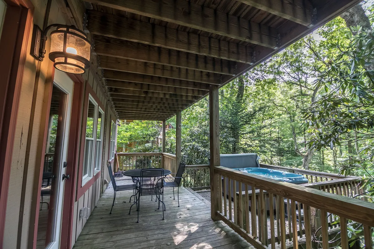 This exterior image features a spacious wooden deck outfitted with an inviting hot tub and comfortable seating area, all set among lush greenery. The scene suggests relaxation and family bonding in a natural setting, with the hot tub being a focal point for unwinding after adventurous days out.