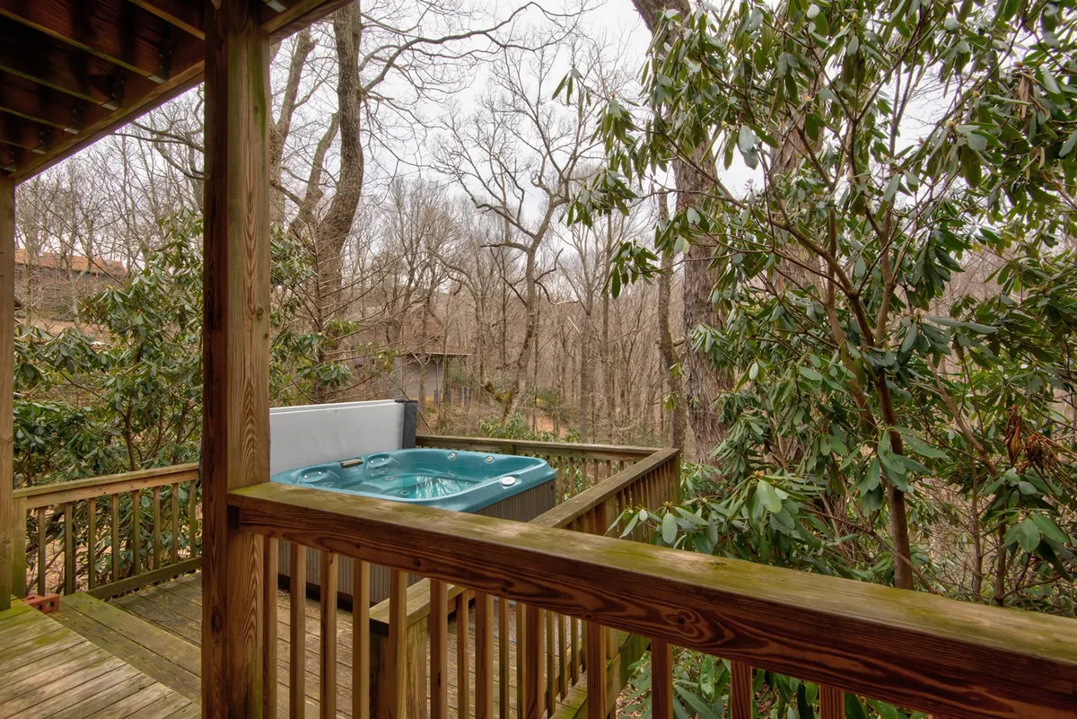A tranquil view of the outdoor hot tub, framed by a wooden railing and leafy foliage. The image highlights the hot tub as a private retreat to unwind after mountain adventures, with nature close at hand.